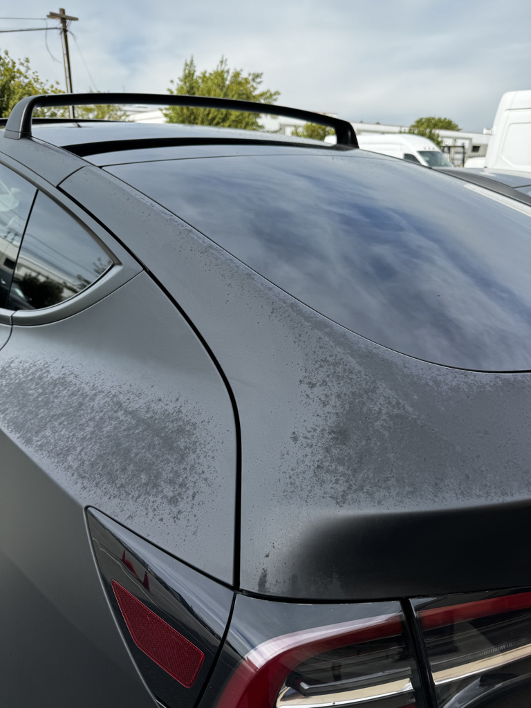 Rear deck and quarter panel with heavy cloudy spotting on an overdue matte wrap