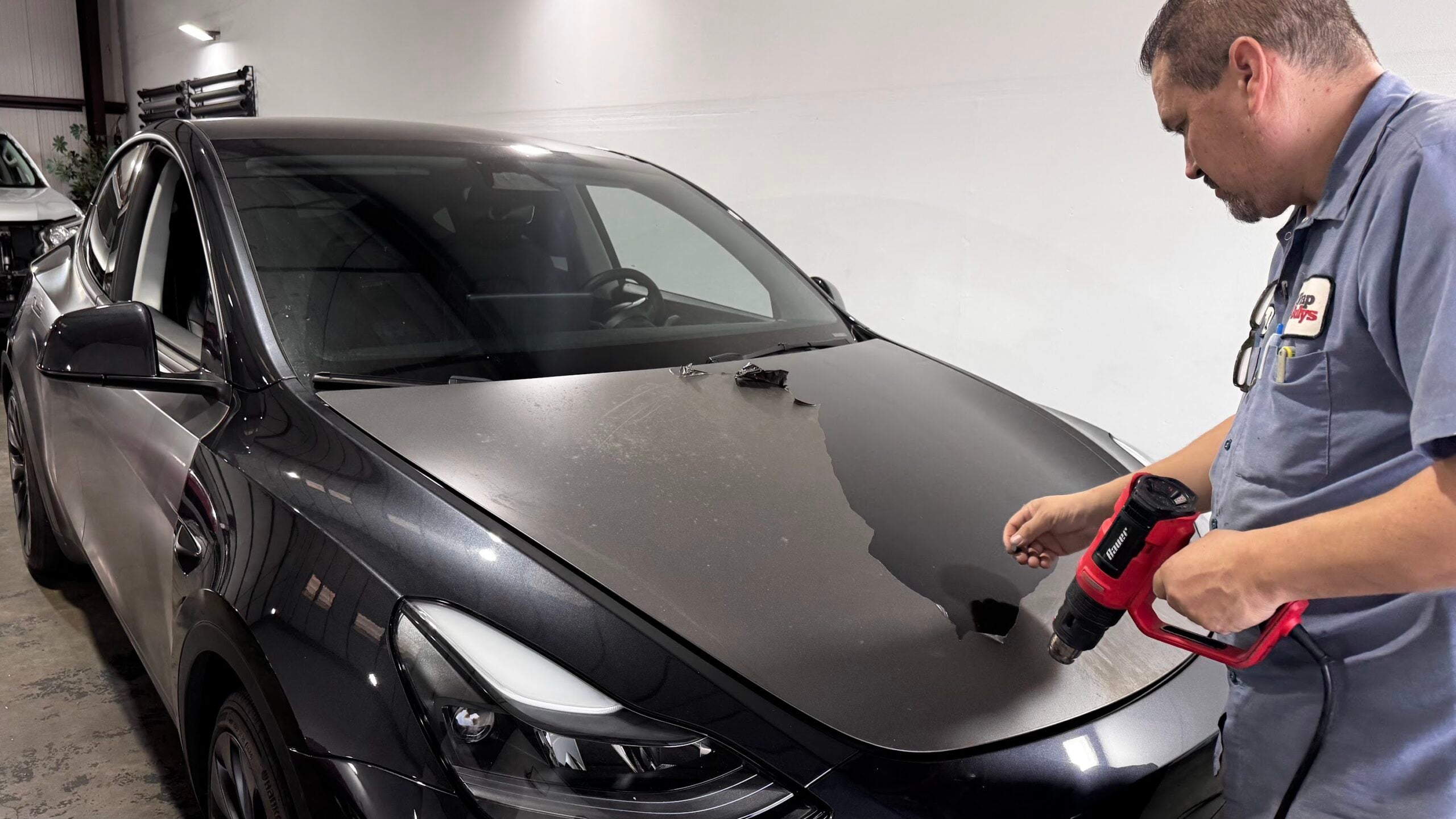 Satin dark gray wrap being removed and revealing glossy factory paint