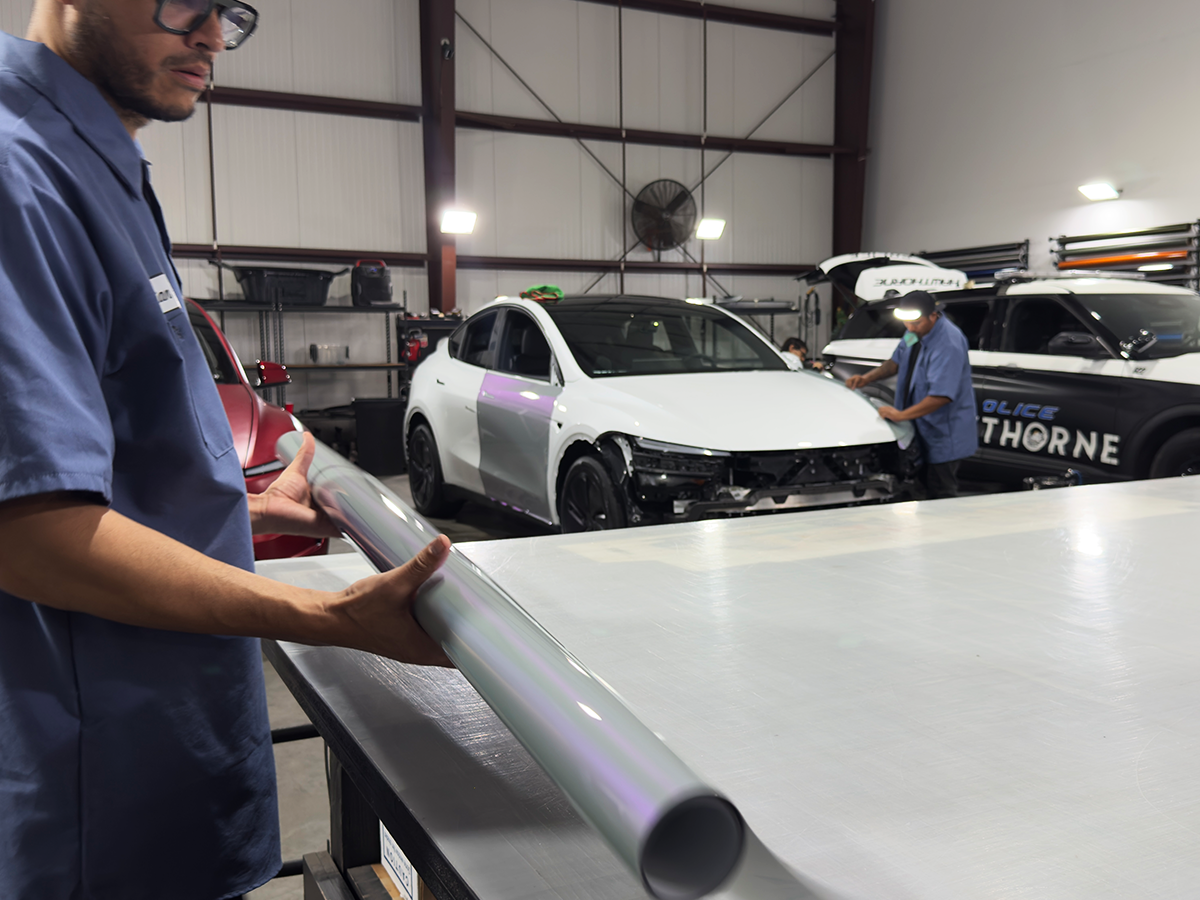 Wrap Bullys technician handling wrap film with active vehicle projects visible throughout the shop